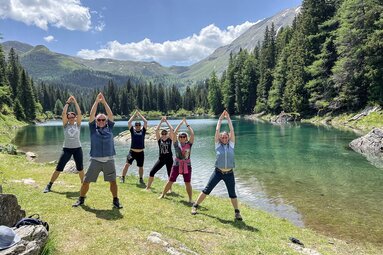Eine Gruppe Menschen in Yoga Pose an einem Bergsee