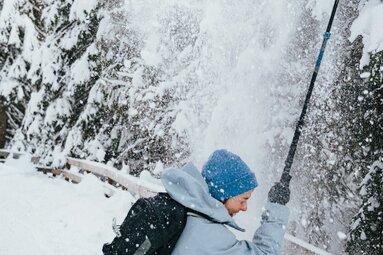 Wędrowiec w rakietach śnieżnych stoi pod mini lawiną drzew i jest zasypany śniegiem | © TVB Wipptal | Johannes Bitter