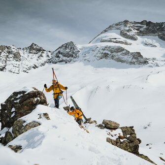Zwei Skitourengeher steigen mit Skiern am Rücken auf einen Berggrat auf | © TVB Wipptal | Johannes Bitter