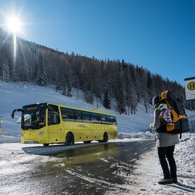Eine Frau wartet mit Rucksack auf den kommenden Skibus | © Tirol Werbung | Sebastian Höhn