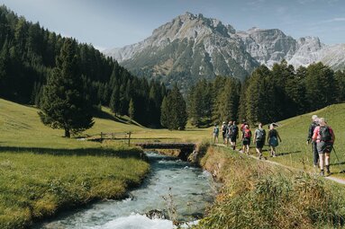 Eine Wandergruppe geht entlang eines kleinen Baches in Obernberg | © TVB Wipptal | Johannes Bitter