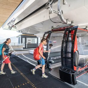 Zwei Frauen mit Wanderausrüstung steigen in eine Gondel ein