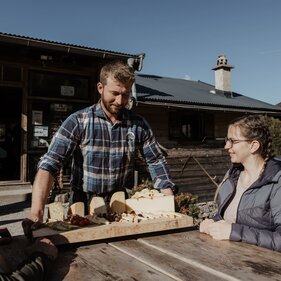Alpine dairyman Thomas Almberger shows two hikers the variety of alpine cheeses | © TVB Wipptal / Victoria Hörtnagl