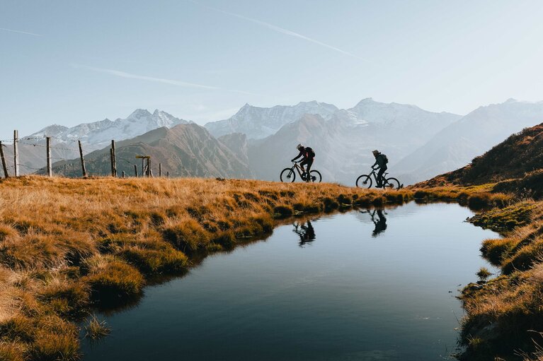 Zwei Biker fahren in herbstlicher Landschaft bei einem Bergsee vorbei | © TVB Wipptal / Johannes Bitter