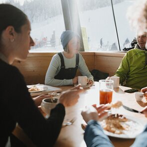 Vier Personen sitzen an einem Tisch vor einem Panoramfenster | © TVB Wipptal | Johannes Bitter